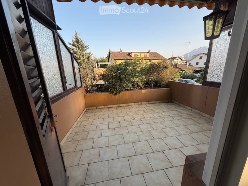 Balcony with tiled floor, beige walls, and a view of surrounding houses and greenery.