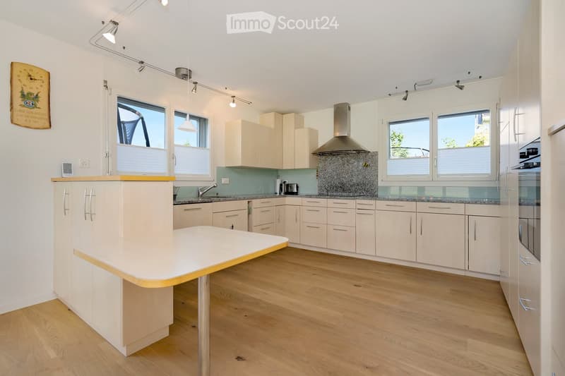 Modern kitchen with light-colored cabinets, a central island, stainless steel appliances, and large windows.