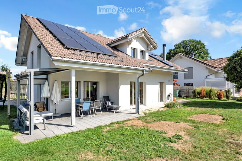 Two-story house with a tiled roof, solar panels, and a covered patio area with outdoor furniture.