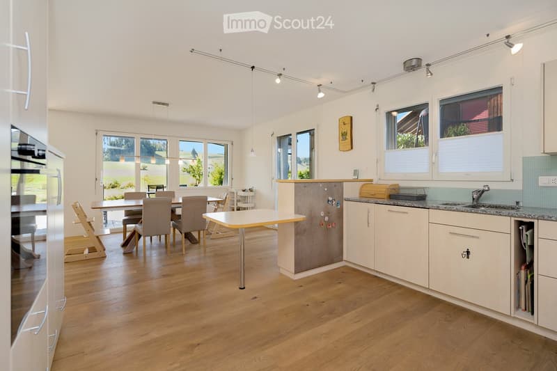 Bright, modern kitchen with white cabinets, granite countertops, and a central island. The space includes a dining area with a table and chairs, a refrigerator, and a sink with a faucet.