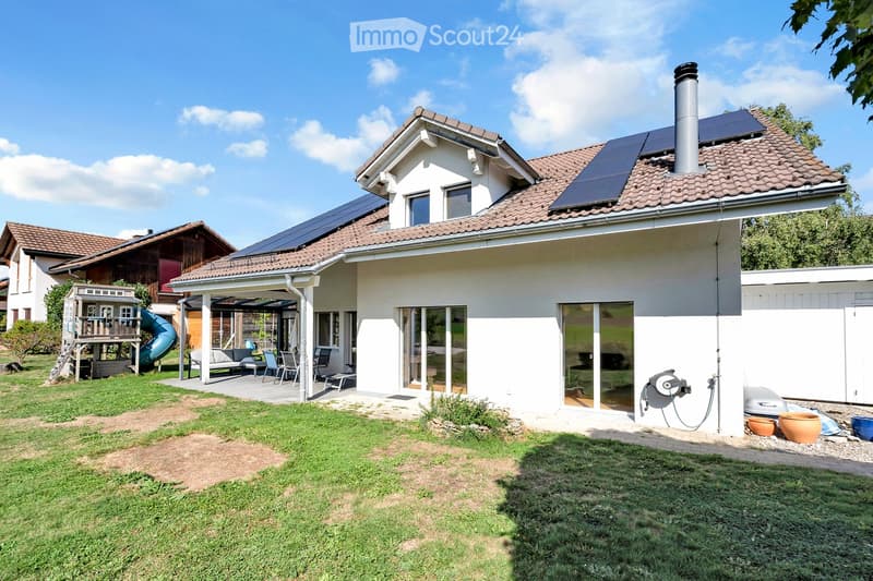 Two-story house with solar panels on the roof, a covered patio area with outdoor furniture, and a well-maintained lawn.