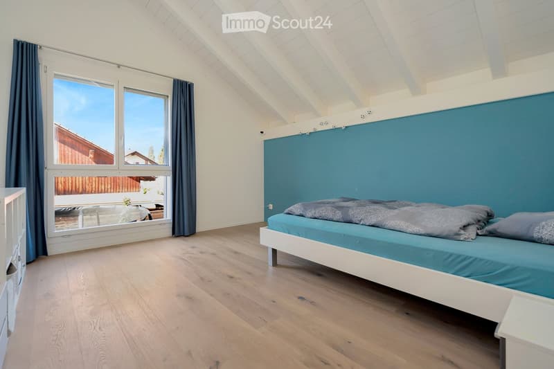 Bright bedroom with wooden flooring, large windows, and a blue accent wall behind the bed.