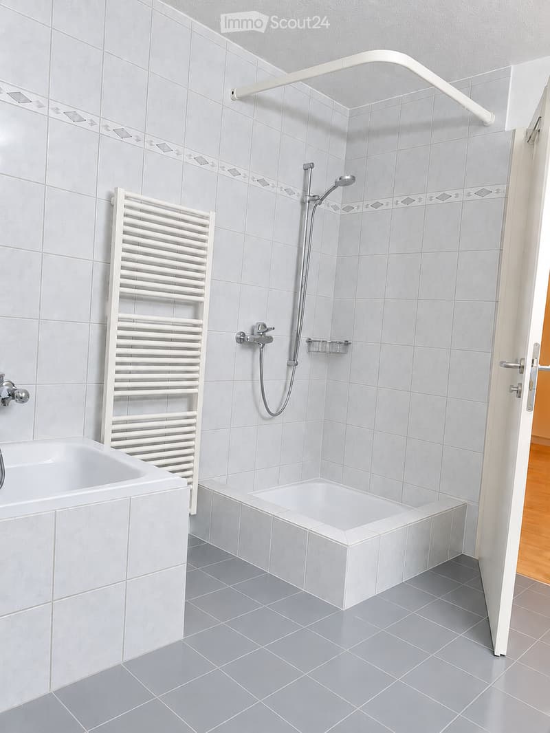 Modern bathroom with grey tiles, a bathtub, a shower area, a white radiator, and a chrome showerhead with handheld sprayer.