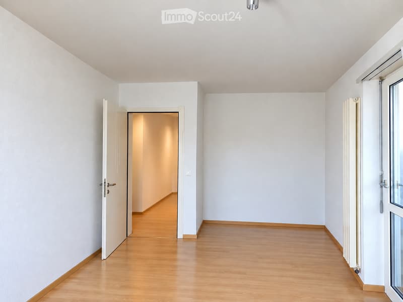 Empty hallway with light wooden flooring, white walls, and a partially open door leading to another room.