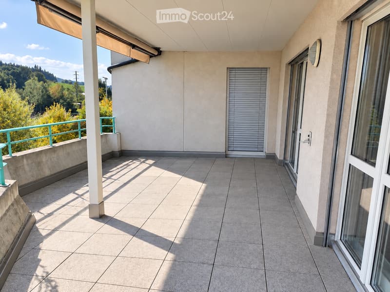Balcony with tiled floor, white walls, large windows, and a scenic view of greenery and hills.