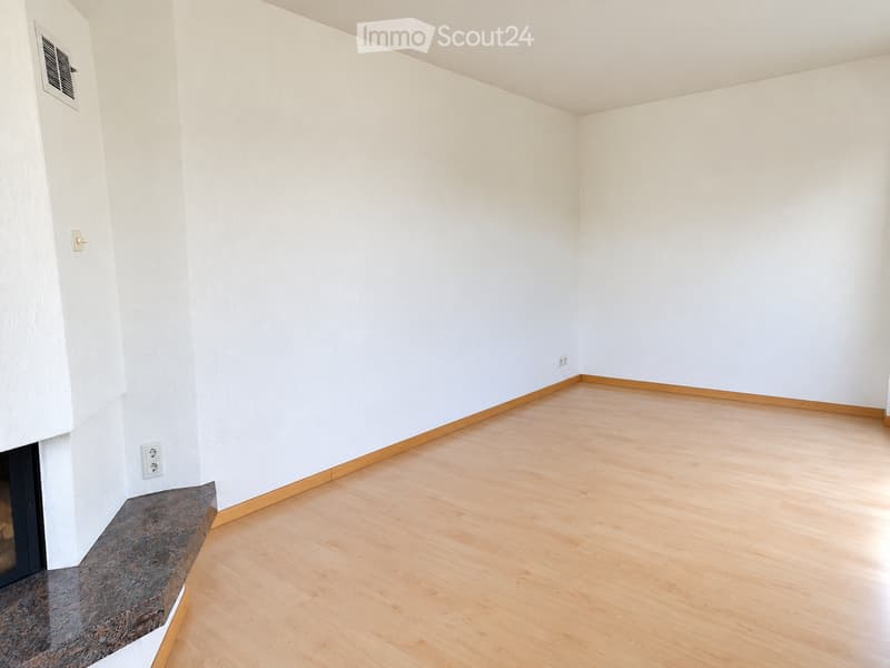 Empty room with light wooden flooring, white walls, and a small fireplace area with a stone mantle.