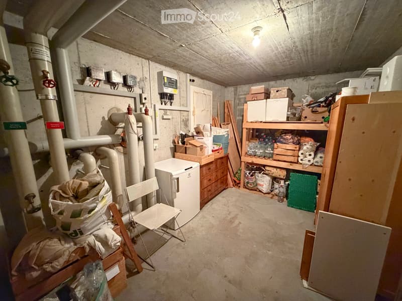 Utility room with exposed pipes, shelves holding various items, a small refrigerator, and a folding chair.