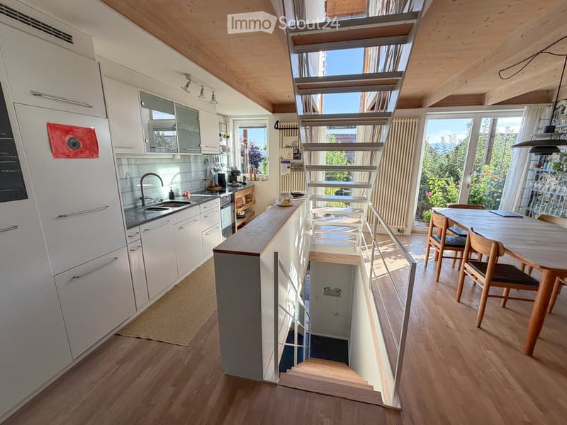 Modern kitchen with white cabinets, wooden floor, and a dining area with a table and chairs. Features a staircase leading to another level.