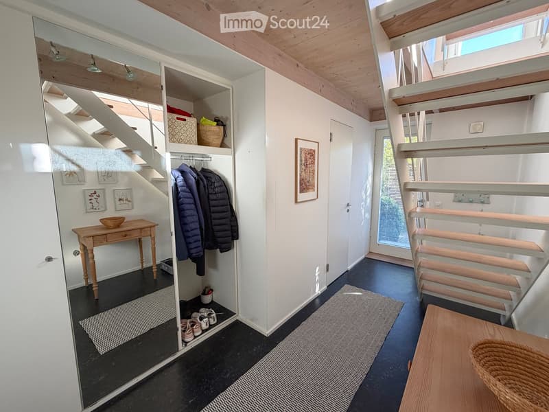 Modern hallway with wooden staircase, built-in closet, small wooden table, and shoe rack. Features exposed wooden beams on the ceiling and a dark blue floor.