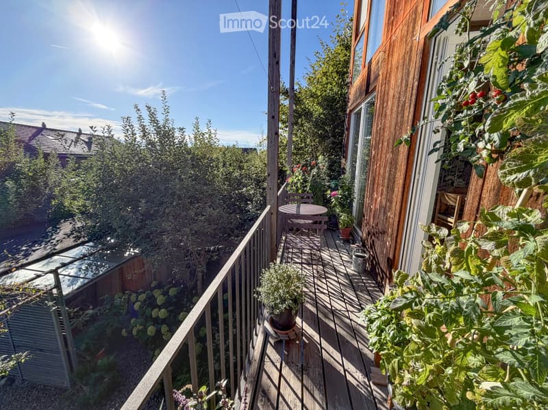 Balcony with wooden decking, metal railing, small round table, two chairs, and potted plants.