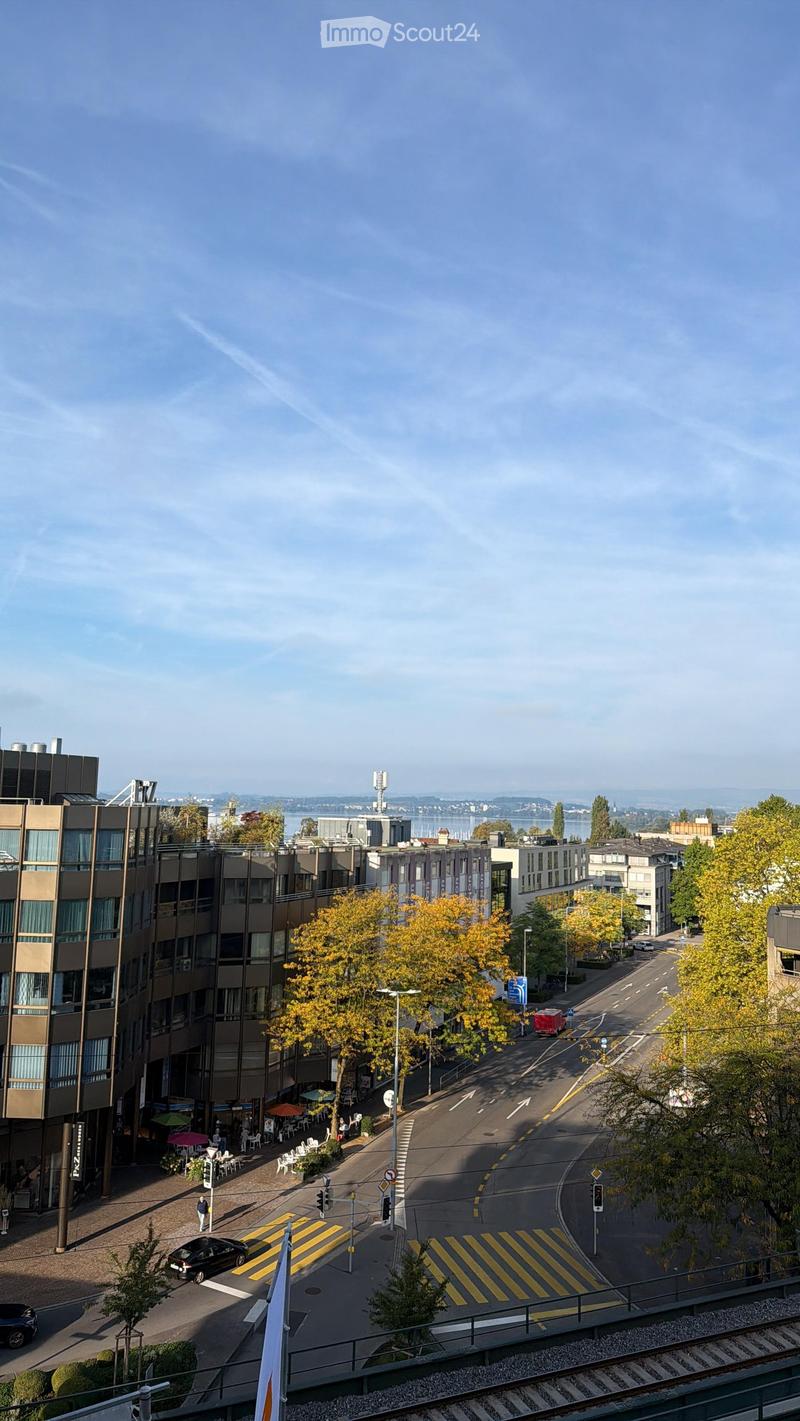 Aerial view of a city street with modern buildings, trees, traffic, and a pedestrian crossing.