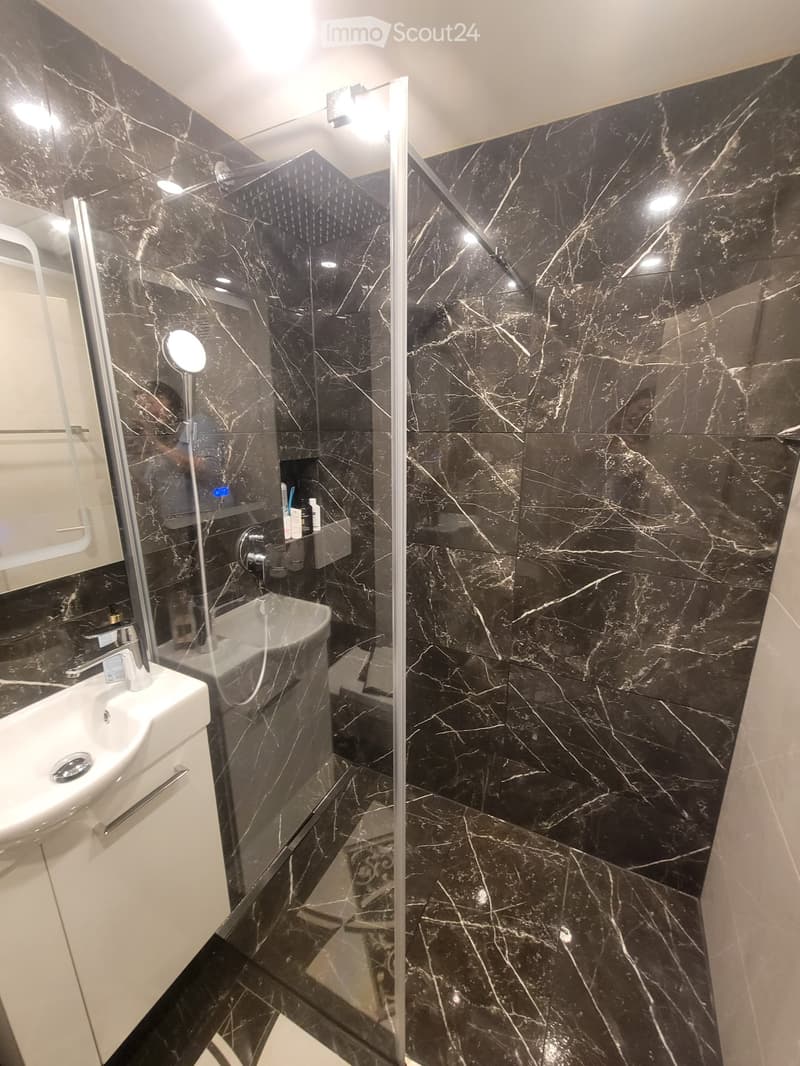 Modern bathroom with black marble tiles, a glass-enclosed shower, a white sink, and a bathtub.