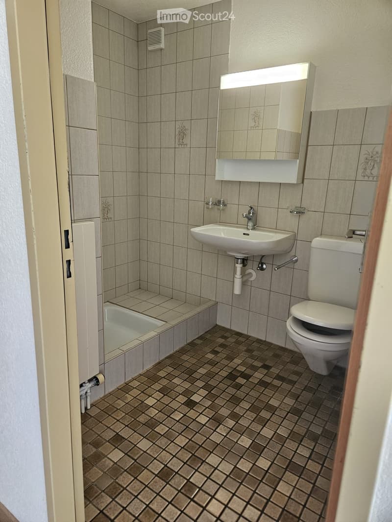 Bathroom with beige tiled walls, a white sink, a toilet, a bathtub, and a mirrored cabinet with a built-in shelf.