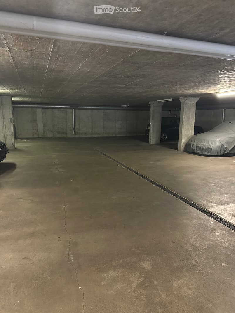 Underground parking garage with concrete floors and walls, featuring a covered car in one bay and visible support columns.