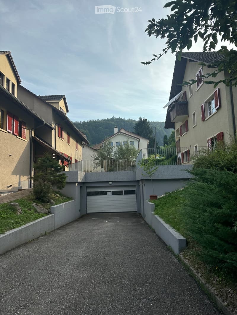 Residential street with multi-story houses, garage, and greenery.