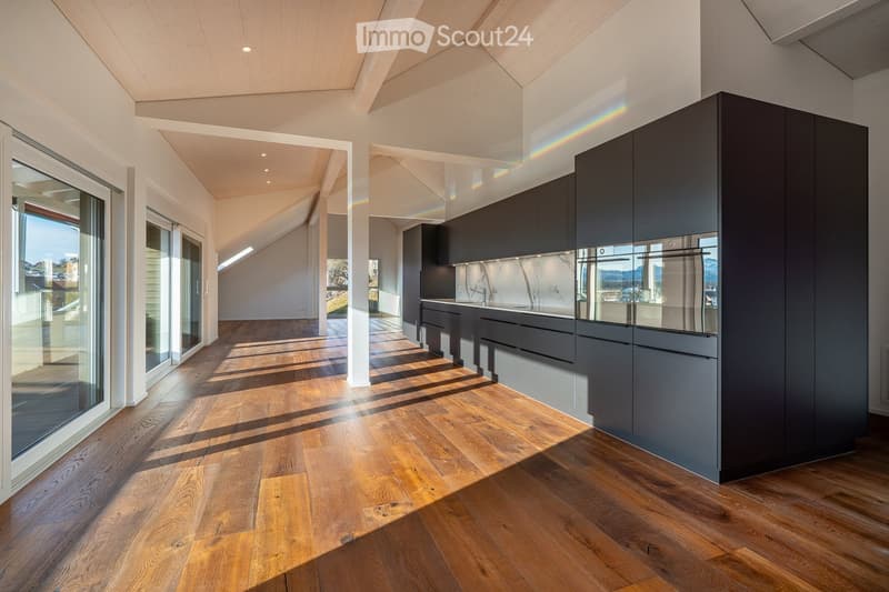 Modern kitchen with dark grey cabinets, a central island, and a sleek sink area. The space features wooden flooring and large windows allowing natural light to flood the room.