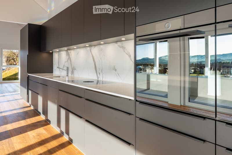 Modern kitchen with sleek, dark cabinets, a marble backsplash, and a large window offering a scenic view.