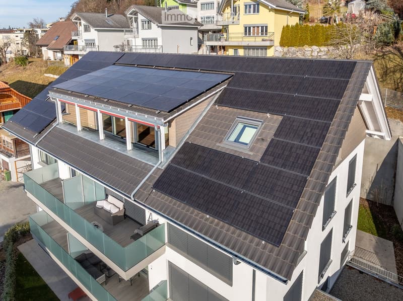 Modern two-story house with solar panels on the roof, large glass balcony, and contemporary design.