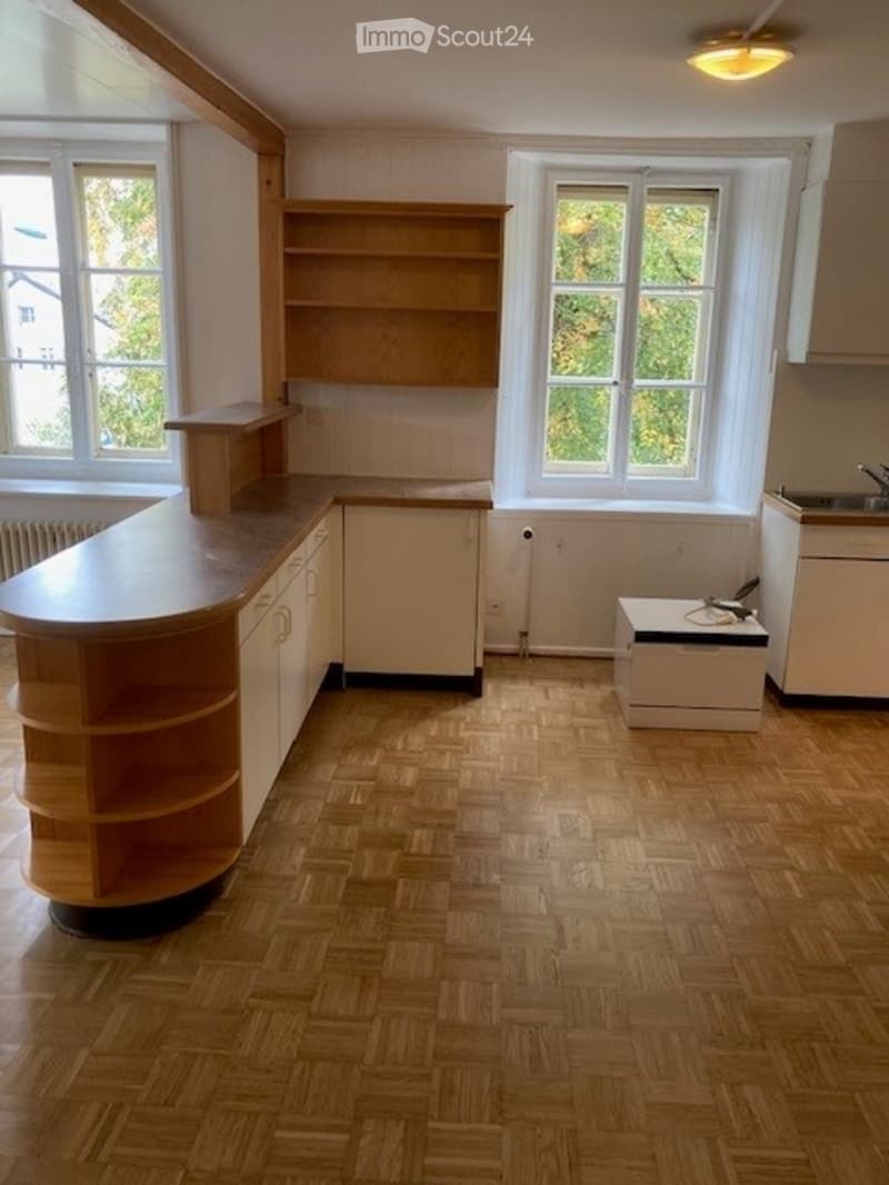 Empty kitchen with wooden flooring, built-in cabinets, and windows. No furniture or appliances are present.