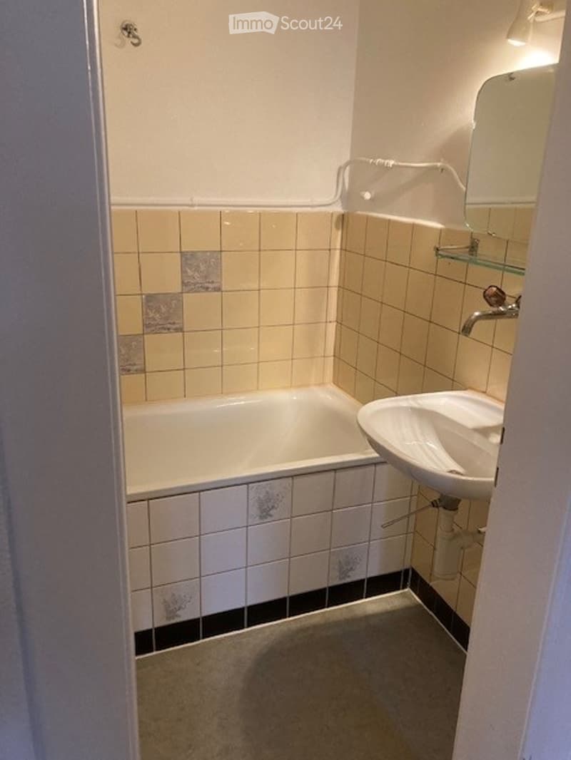 Bathroom with a bathtub, sink, mirror, and tiled walls.