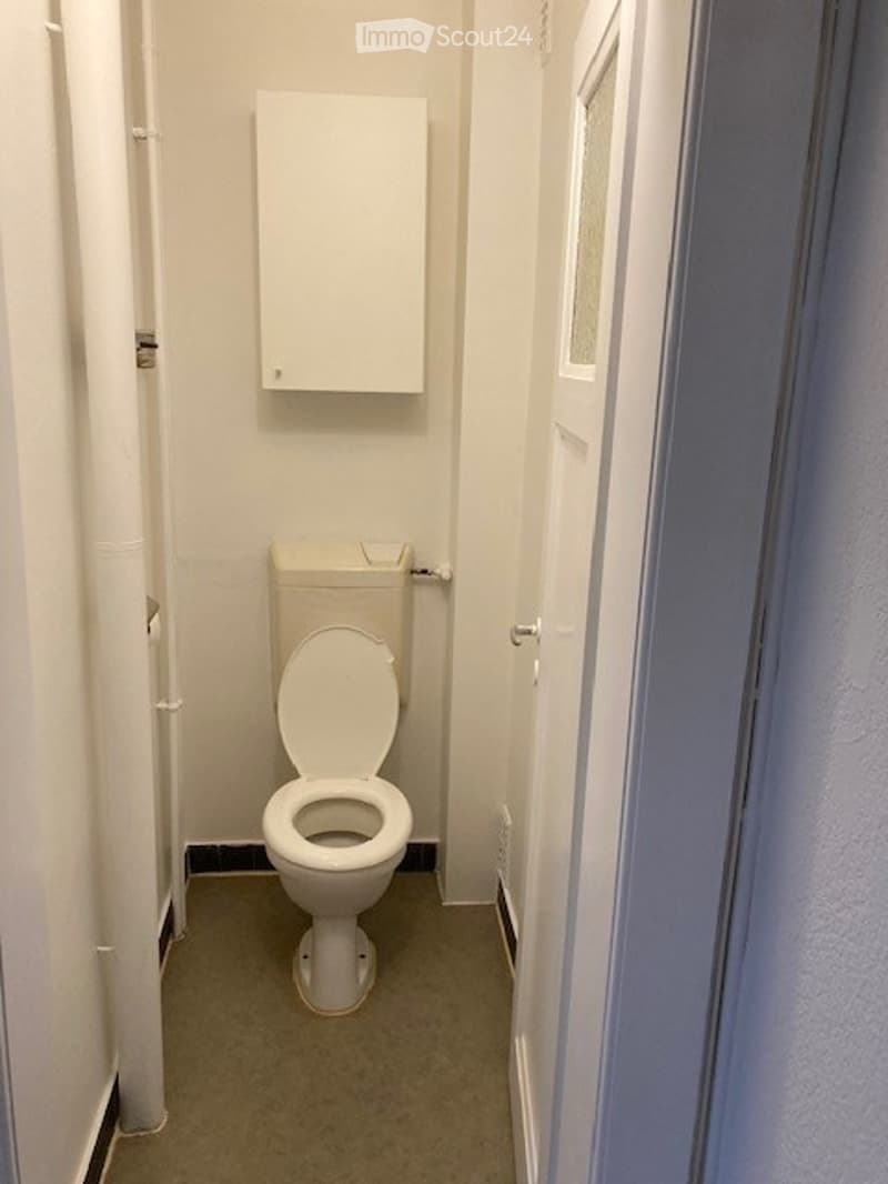 Small bathroom with a toilet and a white cabinet above it. The walls are white, and the floor is a light gray color.