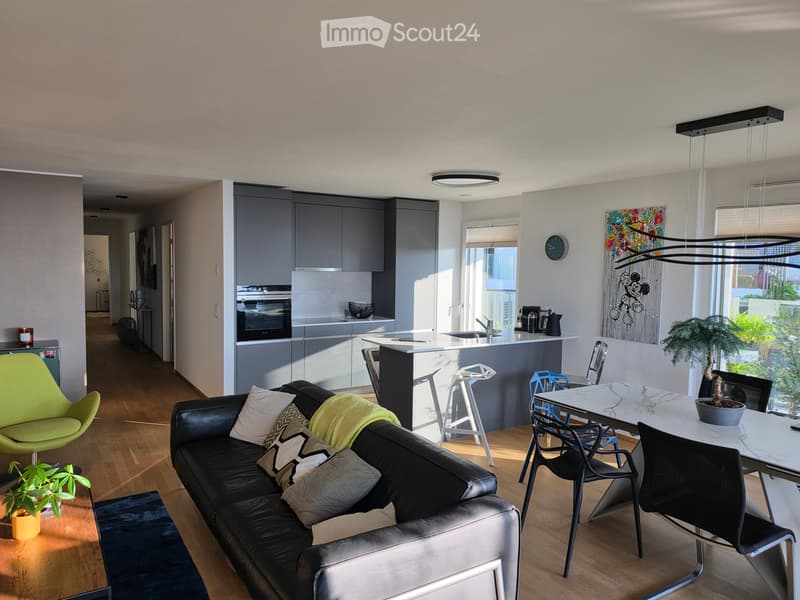 Modern living and dining area with a black leather sofa, green armchair, coffee table, dining table with chairs, kitchen island, and various decorative items.