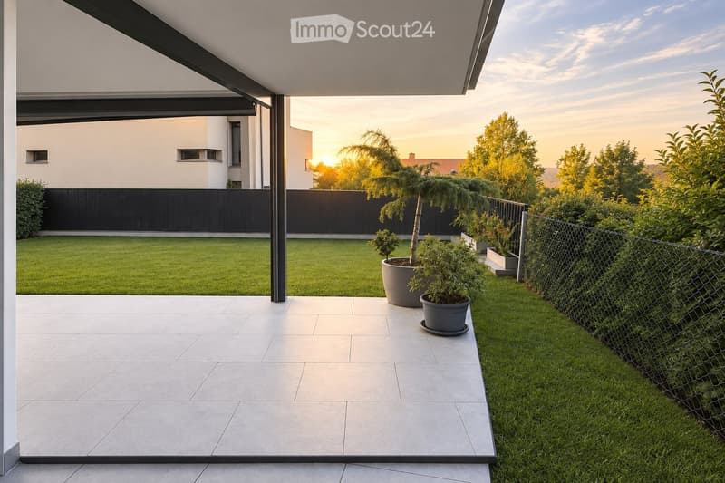 Modern outdoor patio with tiled flooring, potted plants, and a well-maintained lawn, bordered by a metal fence and a contemporary house in the background.