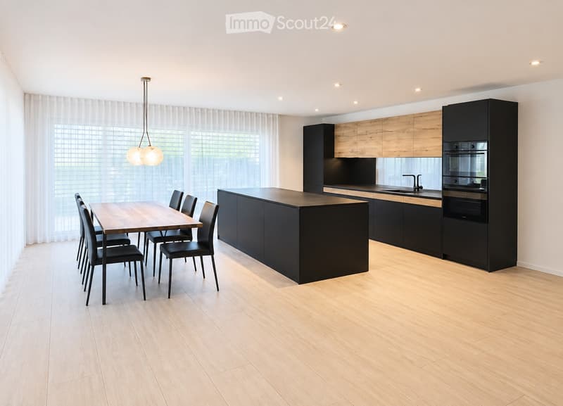 Modern kitchen with a central island, dining area, sleek black cabinets, and wooden flooring.