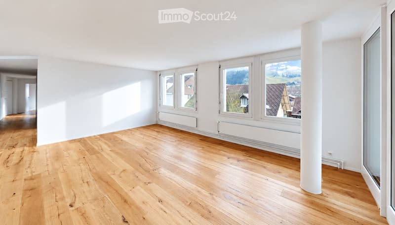 Empty room with light wooden flooring, white walls, large windows, and a white column. No furniture or equipment present.