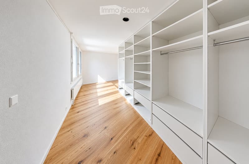 Empty room with wooden flooring, white walls, and built-in white shelving units with drawers and open shelves.