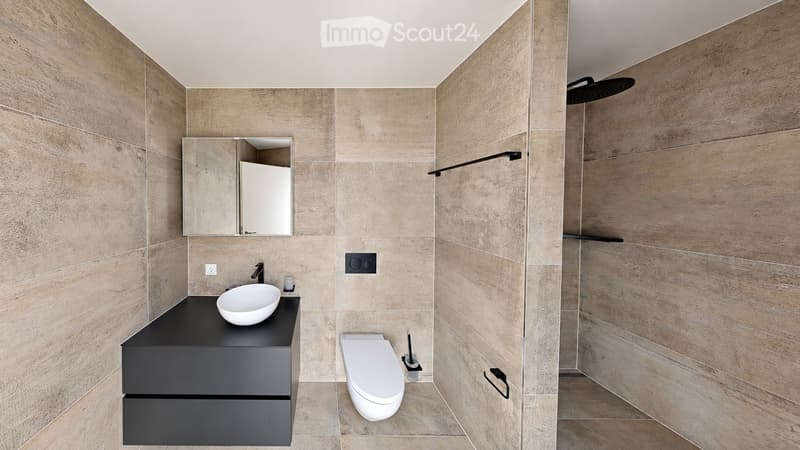 Modern bathroom with beige tiled walls, a black vanity with a white sink, a toilet, and a shower area with a glass enclosure and a black showerhead.