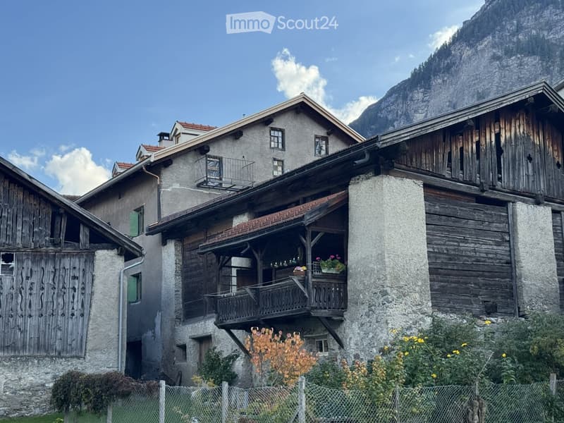 Traditional stone and wooden house with multiple levels, balconies, and a scenic mountain backdrop.