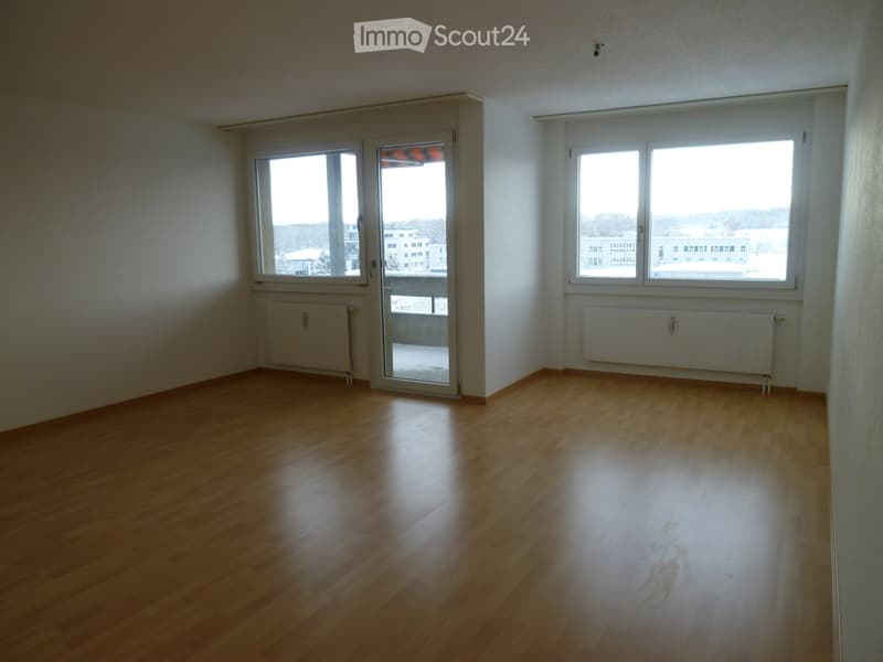 Empty room with wooden flooring, white walls, large windows, and a sliding glass door leading to a balcony.