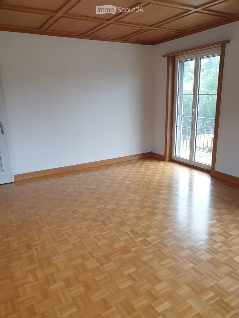 Empty room with wooden herringbone flooring, white walls, and large sliding glass doors leading to a balcony.