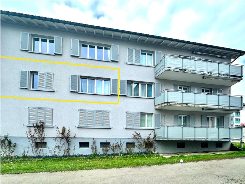 Four-story residential building with multiple windows, shutters, and balconies on the upper floors.