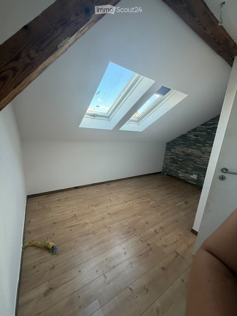 Empty attic space with wooden flooring, white walls, and skylight windows. No furniture or equipment present.