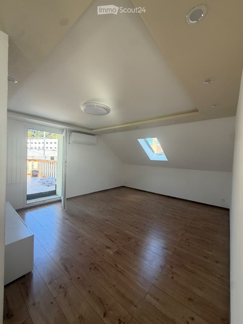 Empty attic room with wooden flooring, white walls, and a skylight window. Features an air conditioning unit and a sliding glass door leading to a balcony.