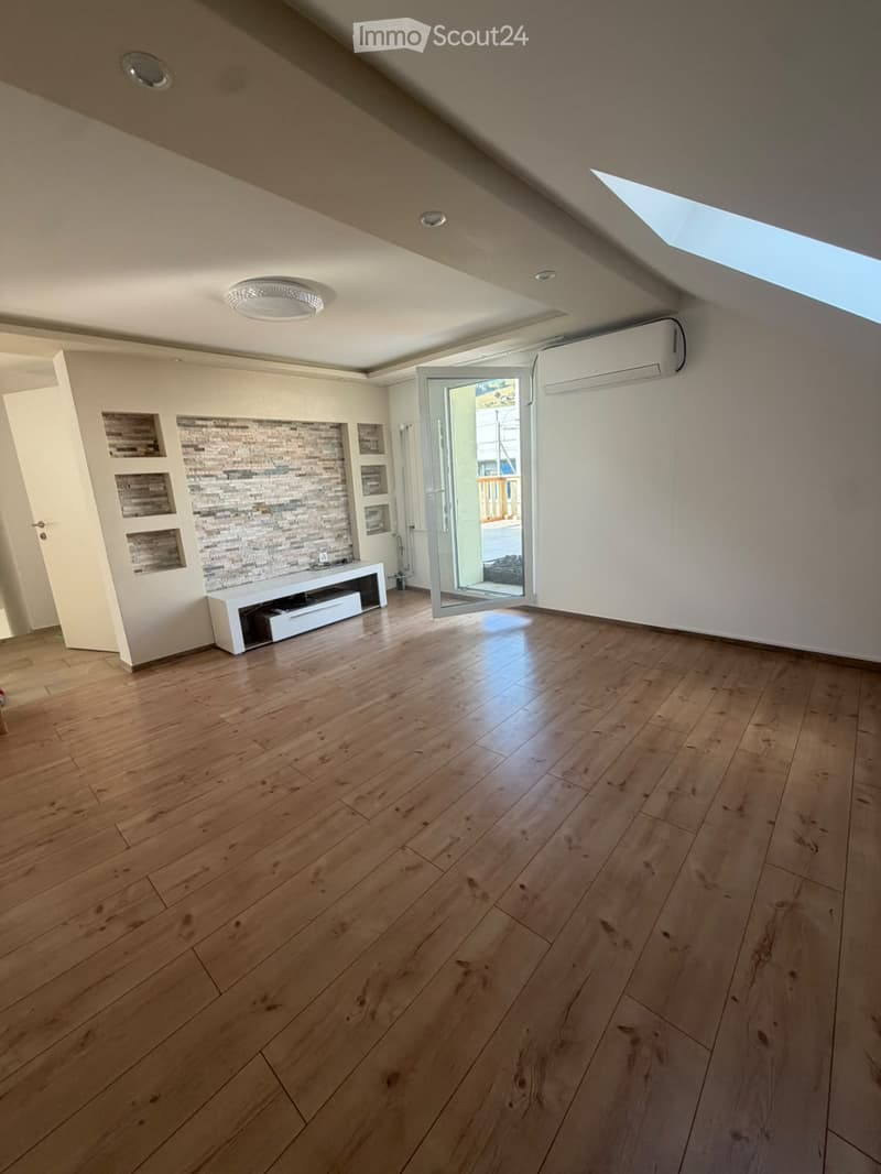 Empty room with wooden flooring, white walls, and a large open door leading outside. Features a modern ceiling light and an air conditioning unit on the wall.