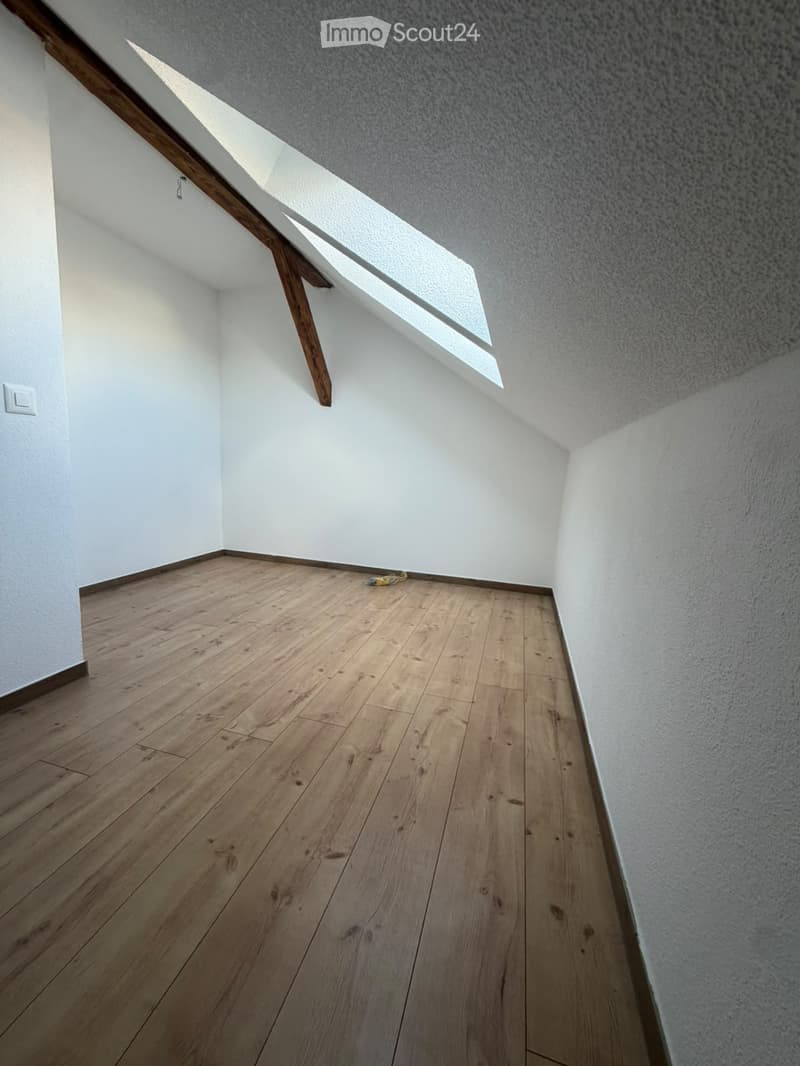 Empty room with wooden flooring, white walls, and a skylight window allowing natural light to enter.