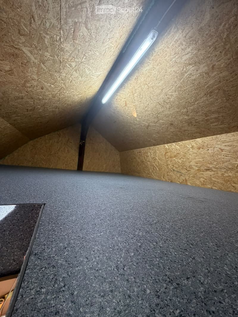 Empty room with wooden walls and a grey carpeted floor, featuring a single built-in LED light fixture on the ceiling.