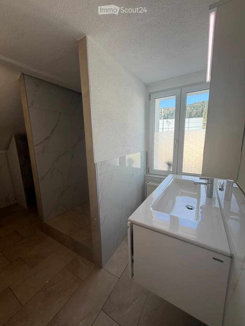 Modern bathroom with a white sink, chrome faucet, and a glass shower enclosure. The room features tiled flooring and a window with a view of the outdoors.