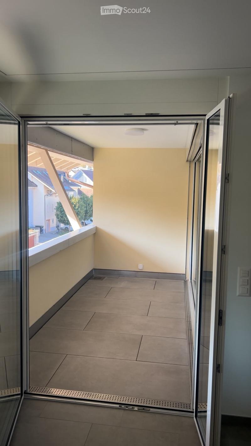Empty balcony with tiled floor, glass railings, and a view of the street and neighboring buildings.