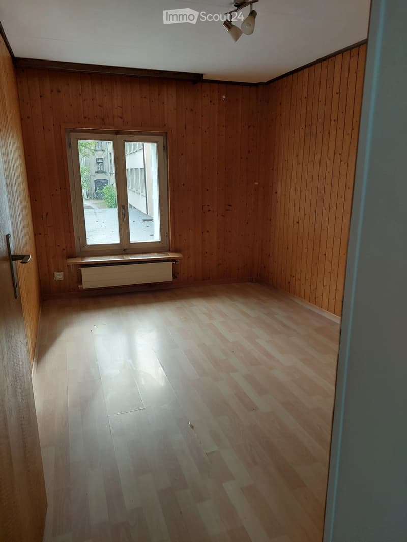 Empty room with wooden walls and flooring, featuring a large window and a door leading outside.
