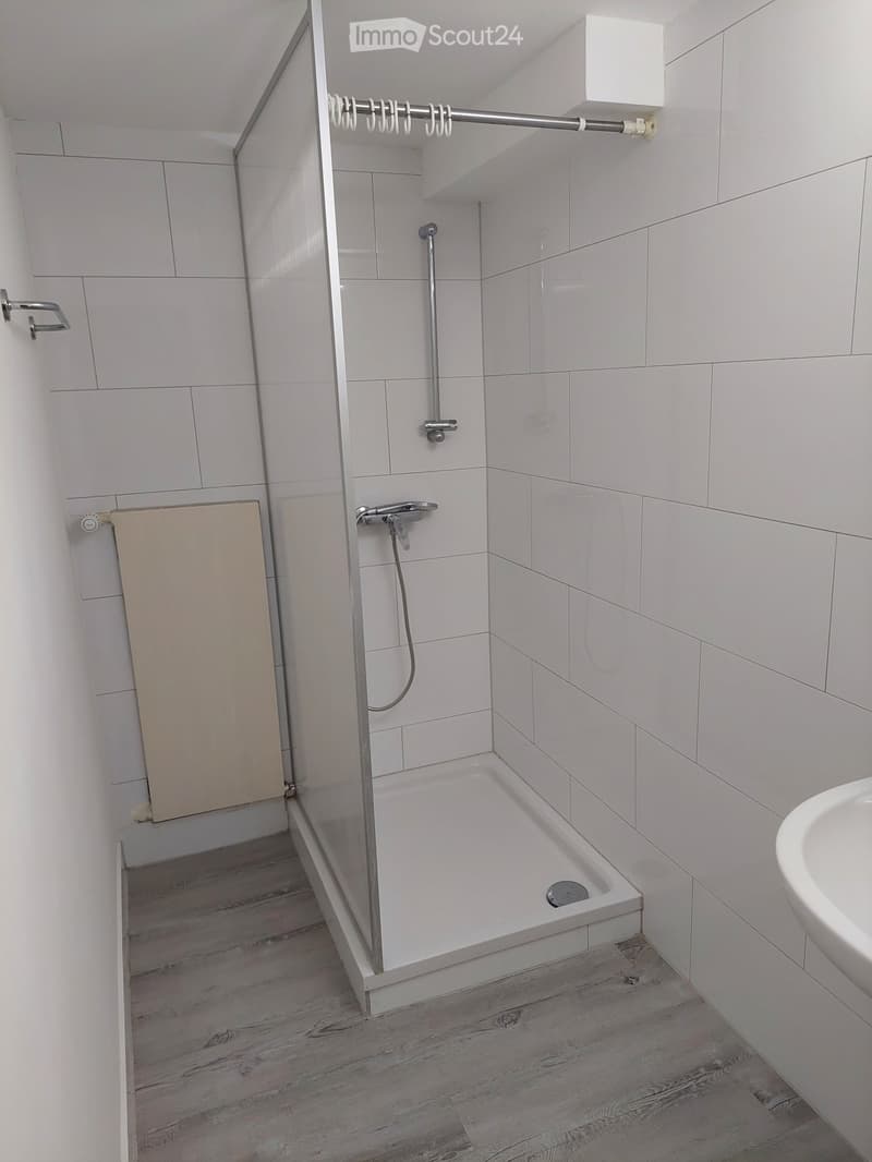 Modern bathroom with white tiled walls, a bathtub with a glass shower enclosure, a sink, and a radiator.