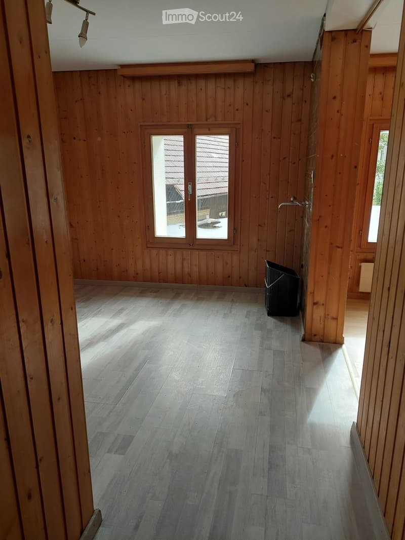 Empty hallway with wooden walls and grey wooden flooring, featuring a large window and a black trash bin in the corner.