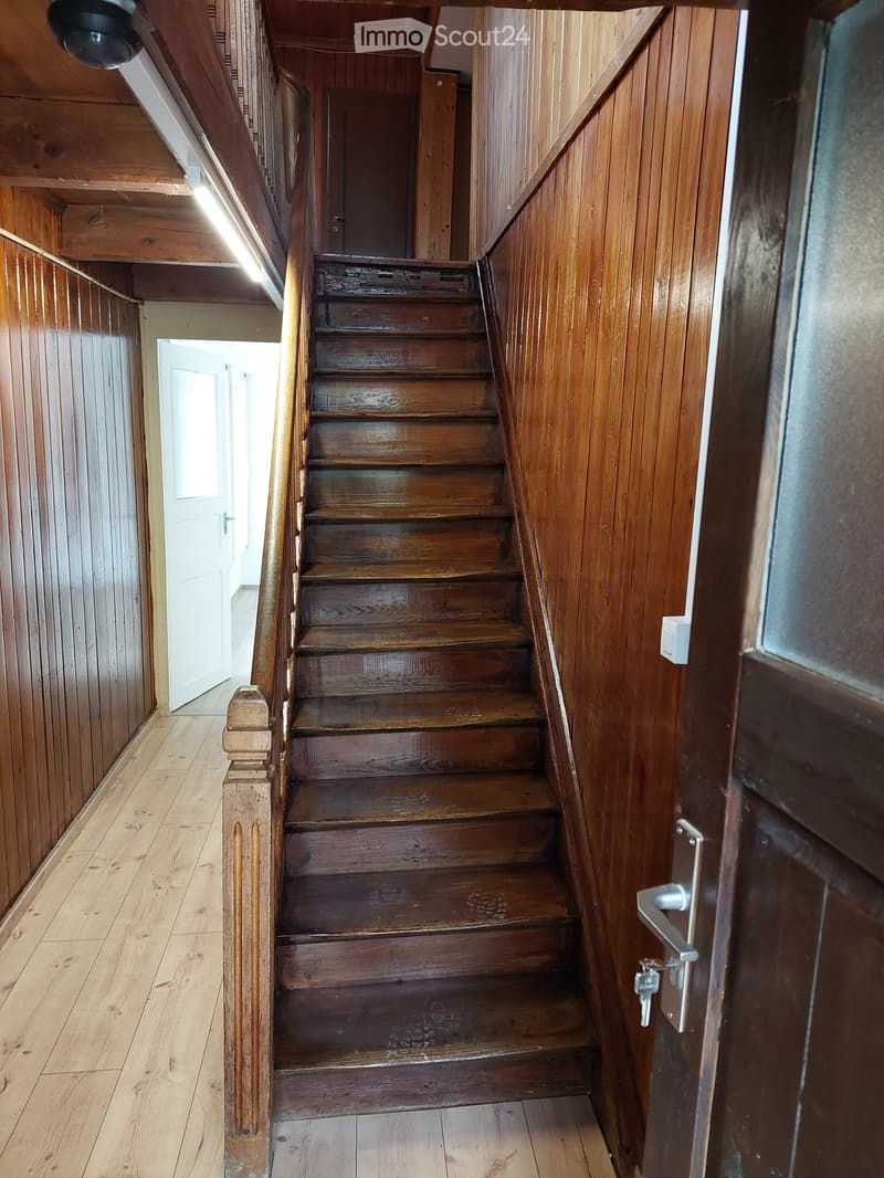 Wooden staircase with polished steps and handrails, leading upwards, flanked by wooden walls and a door at the end.