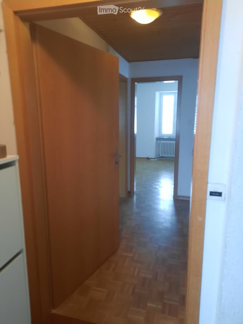 A narrow hallway with wooden doors, tiled floor, and a visible room at the end with a radiator and window.