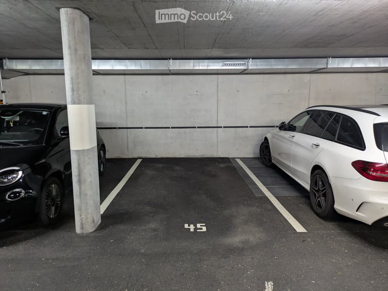 Underground parking area with two parked cars, marked parking spaces, and concrete pillars.