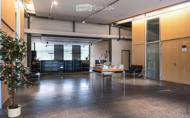 Modern, open-plan reception area with dark tiled flooring, sleek black reception desk, contemporary chairs, a small table, and a potted plant.