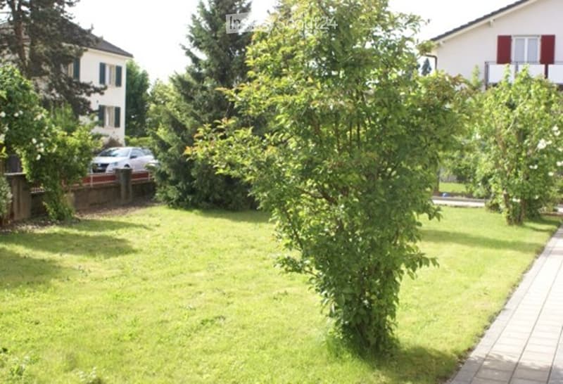Well-maintained garden with green lawn, trees, and a parked car in the driveway.